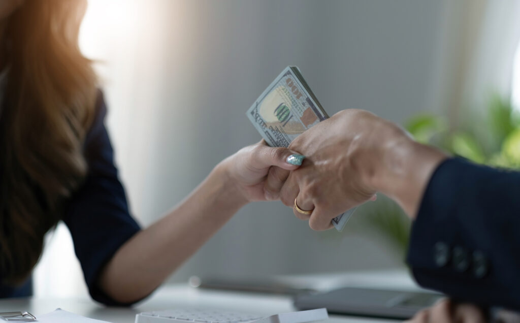 Hands exchanging US dollar bills in a financial transaction.