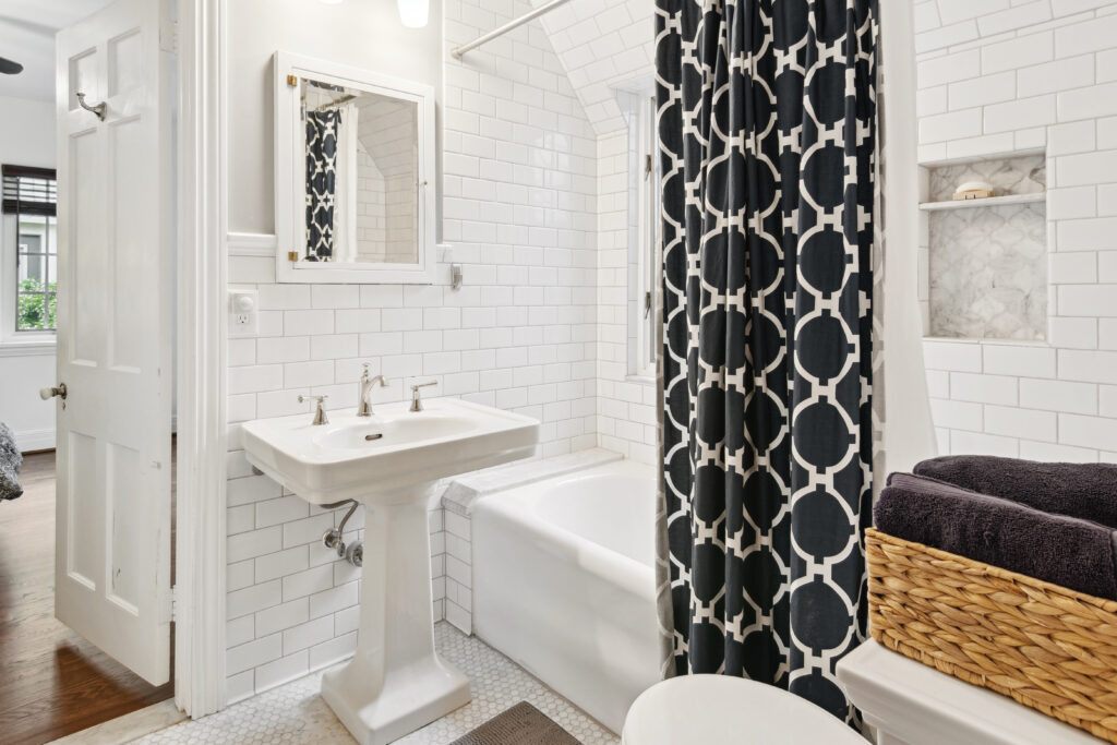 Bright white bathroom with classic fixtures and patterned shower curtain.