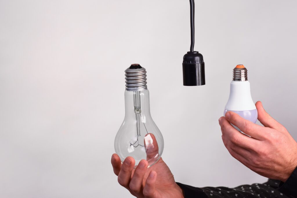 Hand holding a clear light bulb near a black socket and a white bulb.