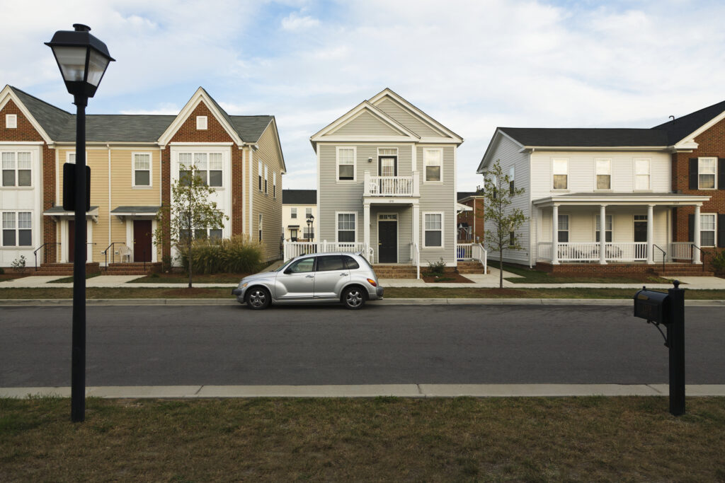 Three modern houses with a car parked in front on a sunny day.