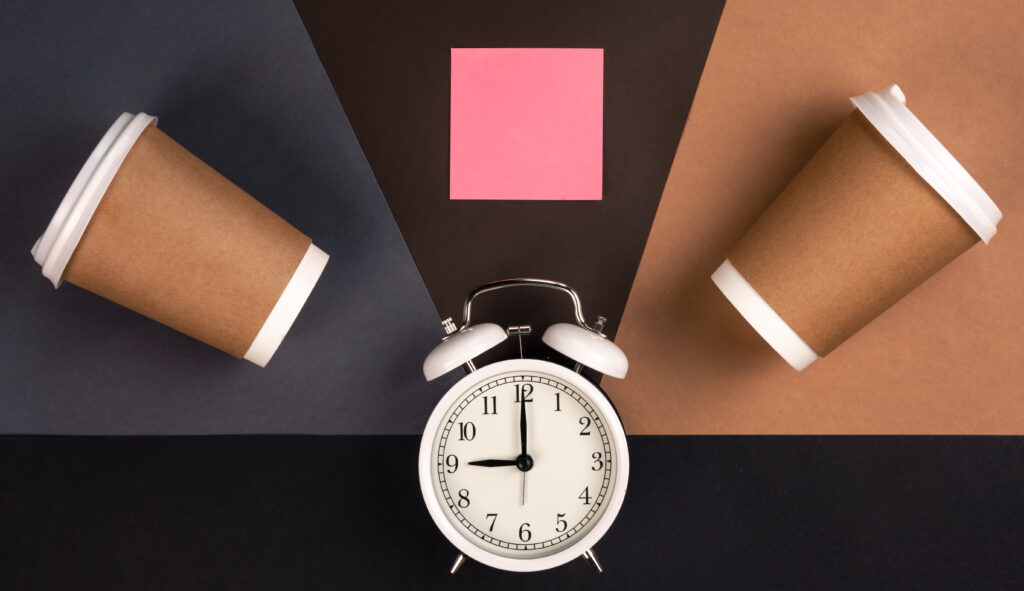 Two coffee cups and an alarm clock with a blank pink sticky note.