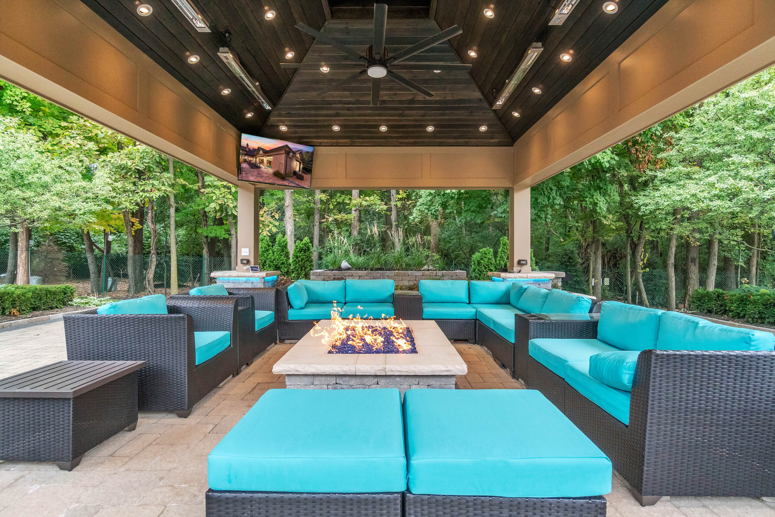 Modern outdoor lounge with turquoise seating and a central fire pit under string lights.