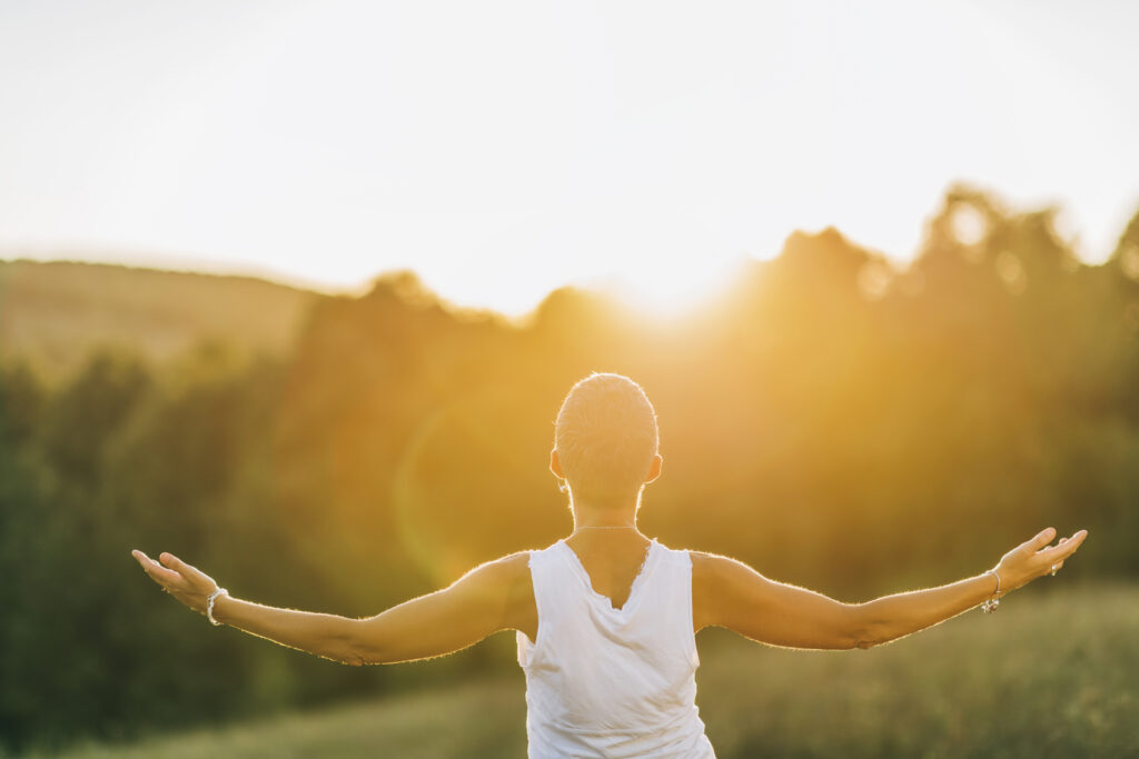Person stretching arms outdoors at sunrise or sunset.
