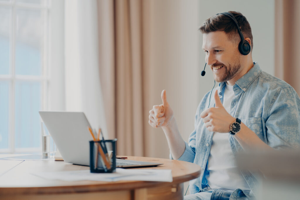 Man with headset giving thumbs up while working on laptop.