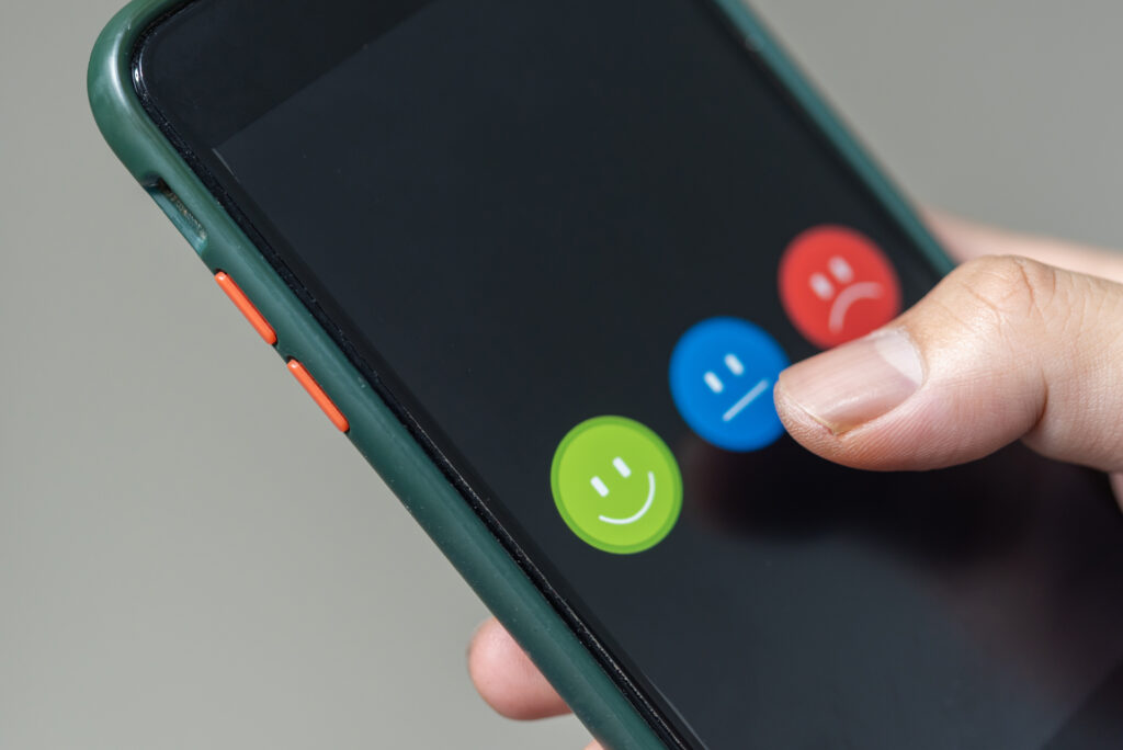 Finger selecting a neutral emoji on a smartphone screen.