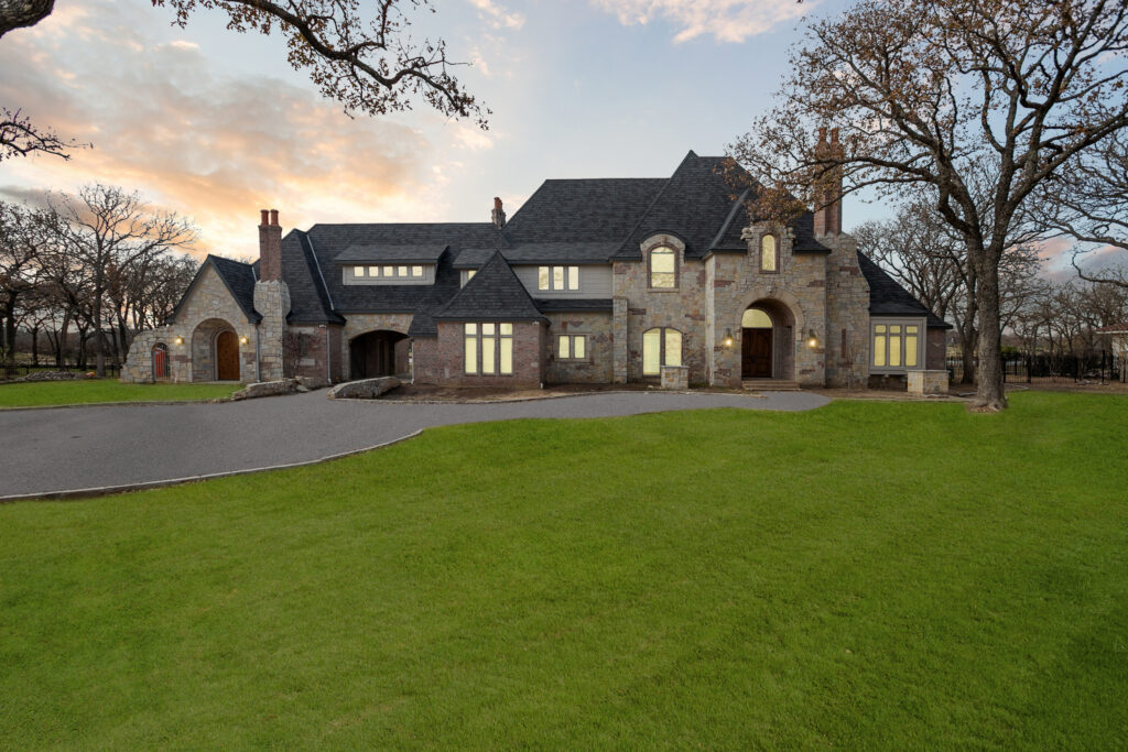 Large elegant stone house with manicured lawn at sunset.
