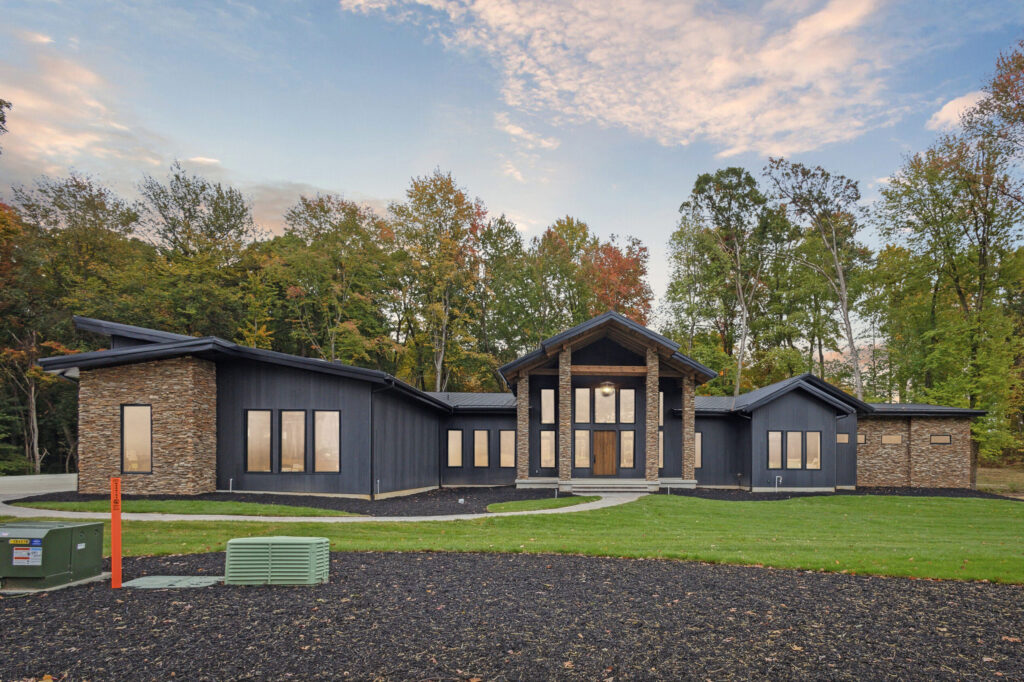 Modern single-story house with large windows and wood accents surrounded by trees.