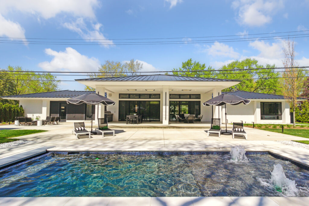 Modern house with a swimming pool and outdoor lounge area under a bright sky.