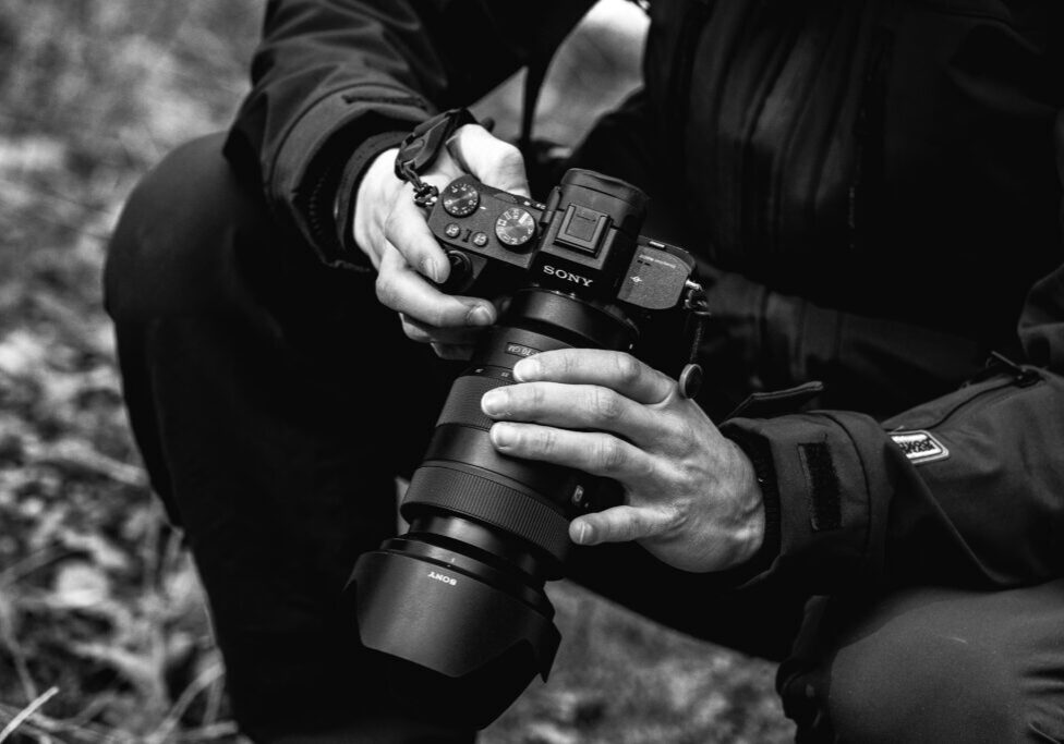 Close-up of a person adjusting a professional camera outdoors.